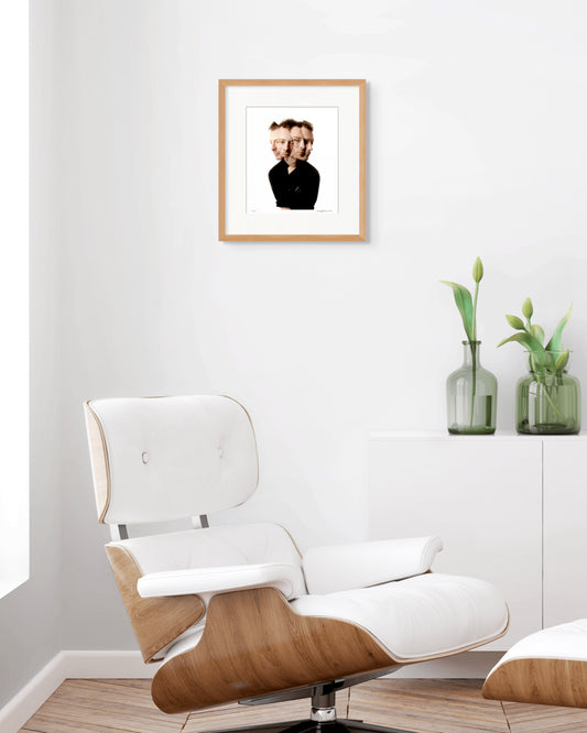 Framed Thom Yorke portrait by Robin Sellick displayed above a white Eames-style chair and tulip vases – modern, minimalist and refined.