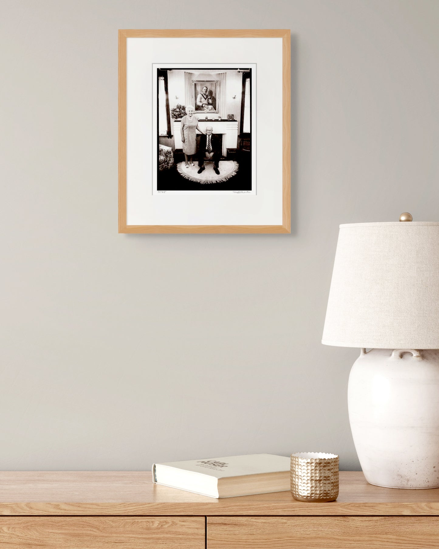 Framed Bradman portrait by Robin Sellick styled with neutral lamp and book – refined, contemporary collector setting.