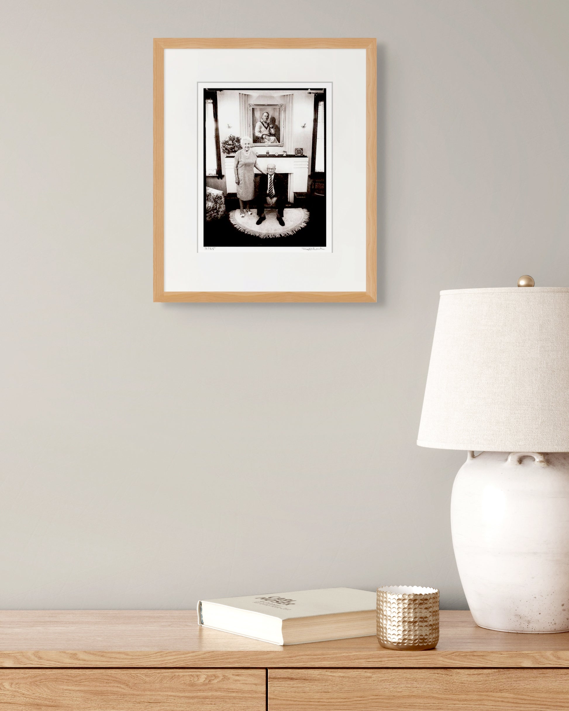 Framed Bradman portrait by Robin Sellick styled with neutral lamp and book – refined, contemporary collector setting.