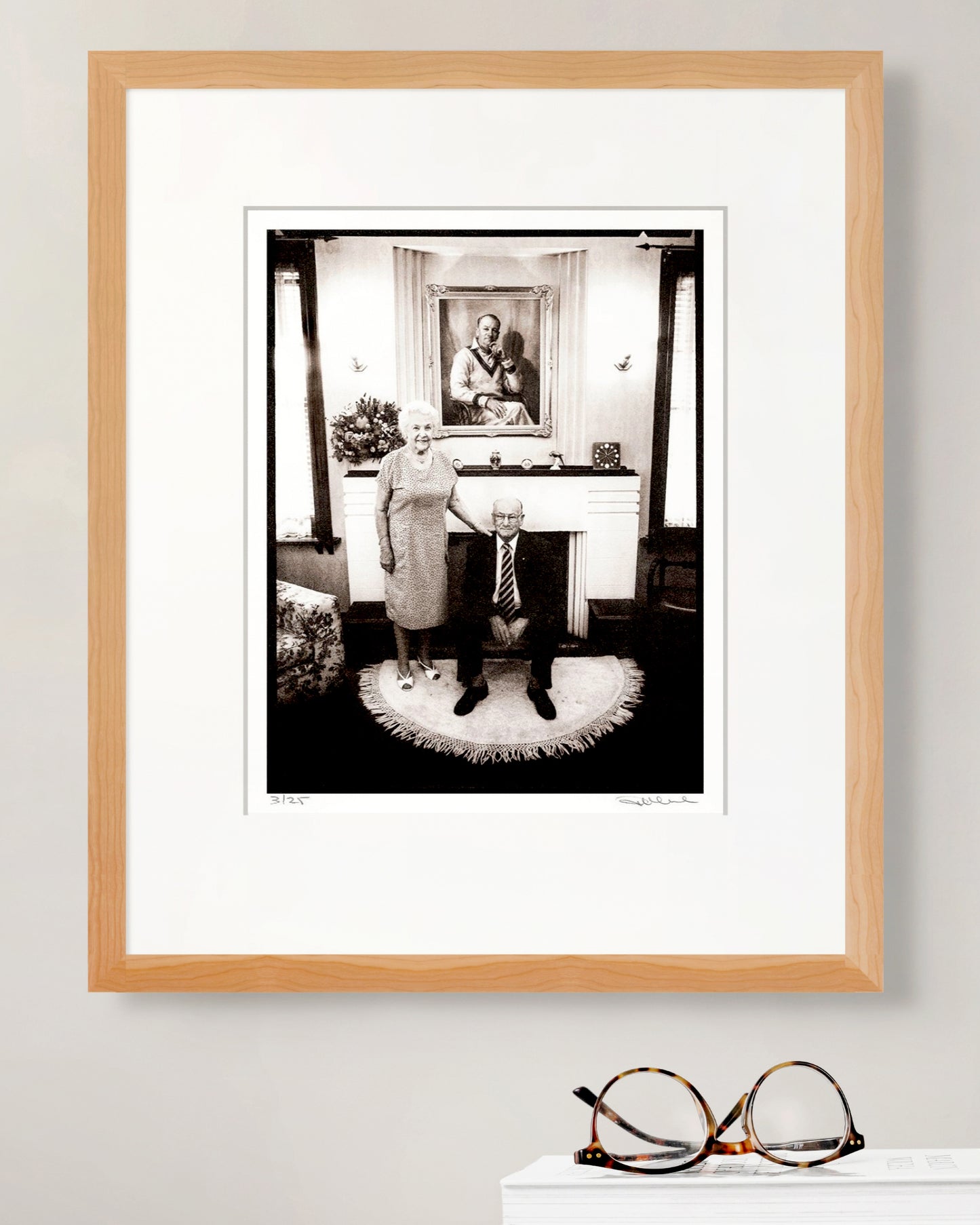 Framed limited edition portrait of Sir Donald and Lady Jessie Bradman by Robin Sellick beside tortoiseshell glasses – elegant collector display celebrating Australian sporting heritage.