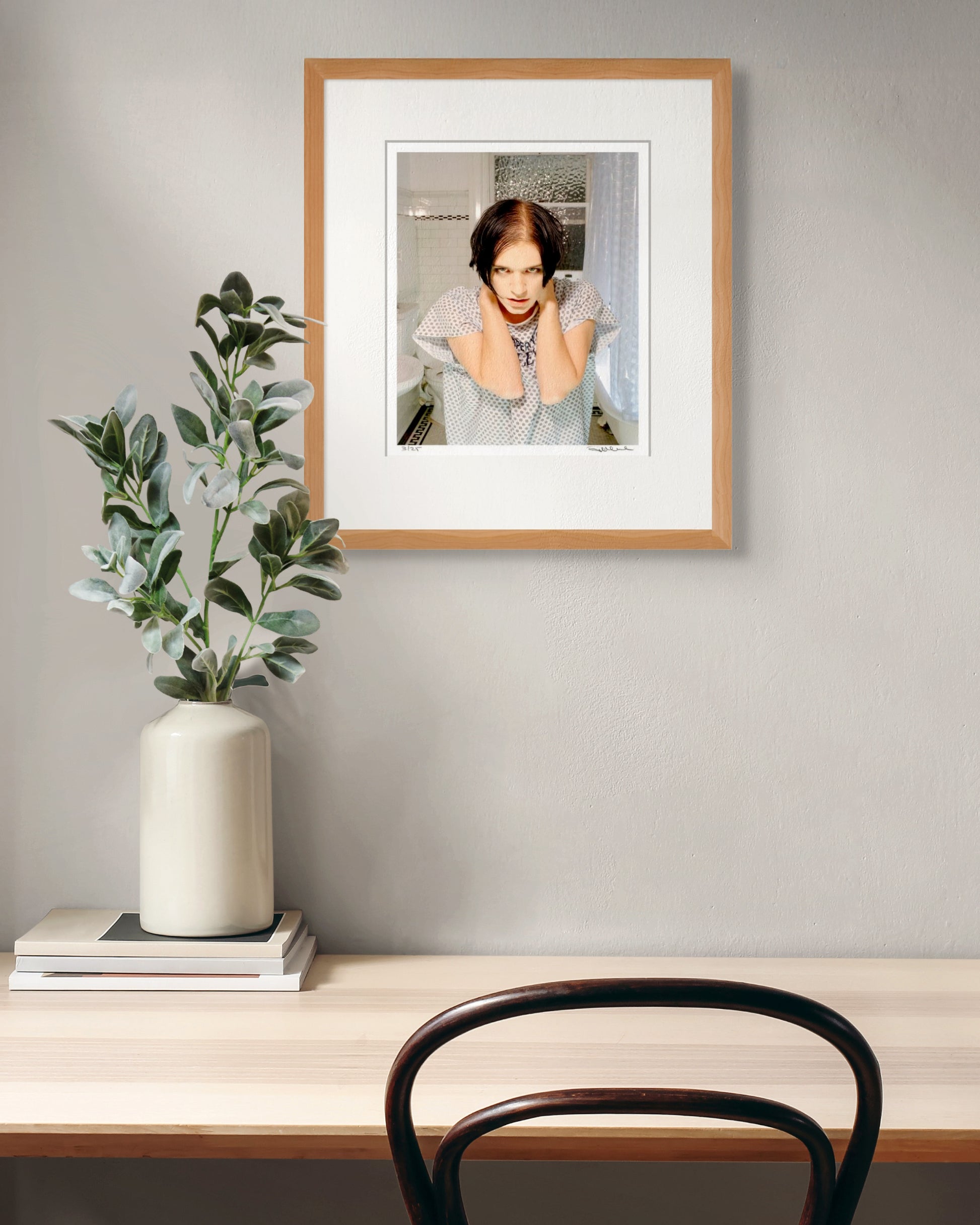 Framed Brian Molko portrait by Robin Sellick displayed above a minimal desk with green foliage – striking art for modern interiors.