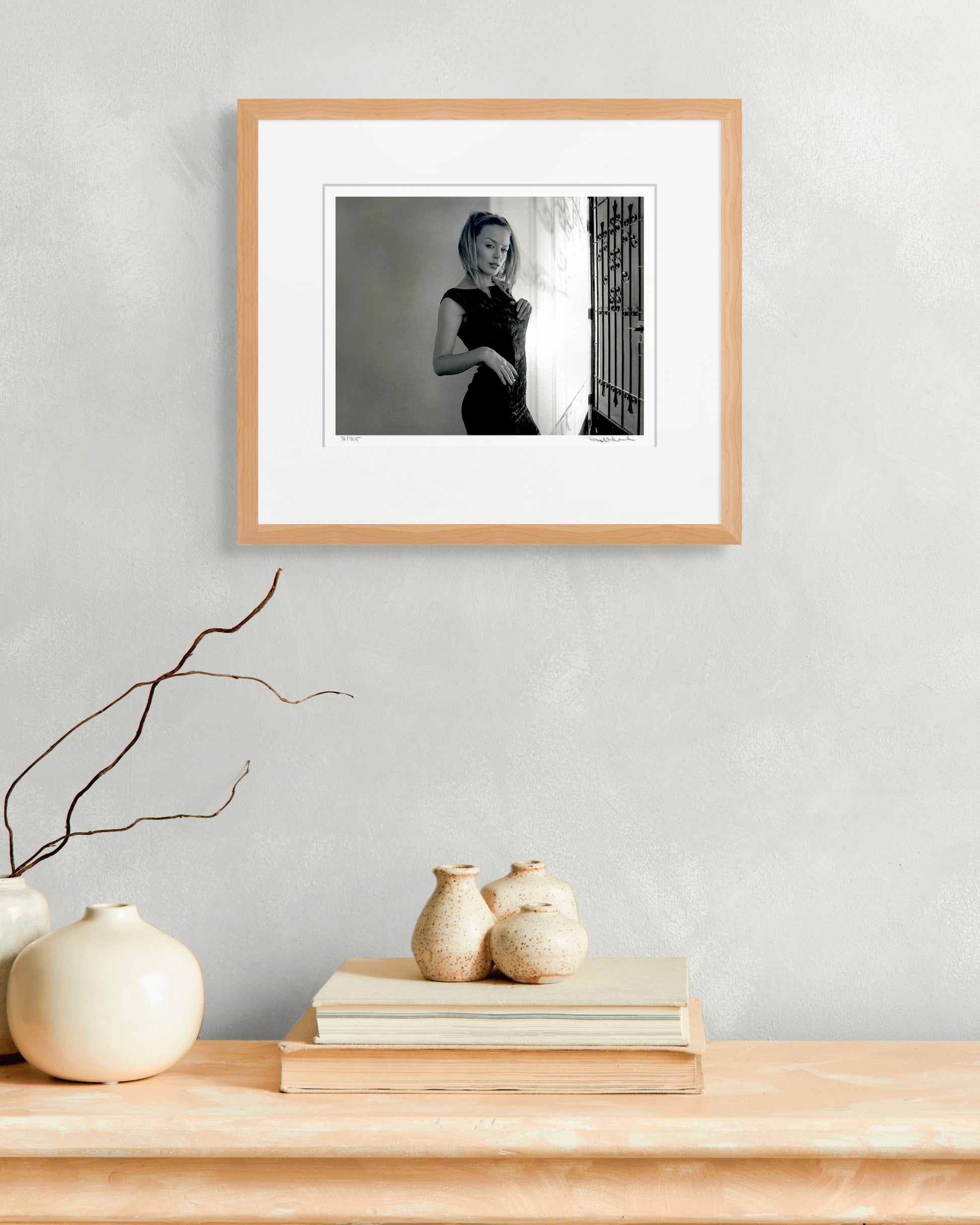 Framed limited-edition Kylie Minogue portrait by Robin Sellick above stacked books and ceramic pots – refined collector interior styling.