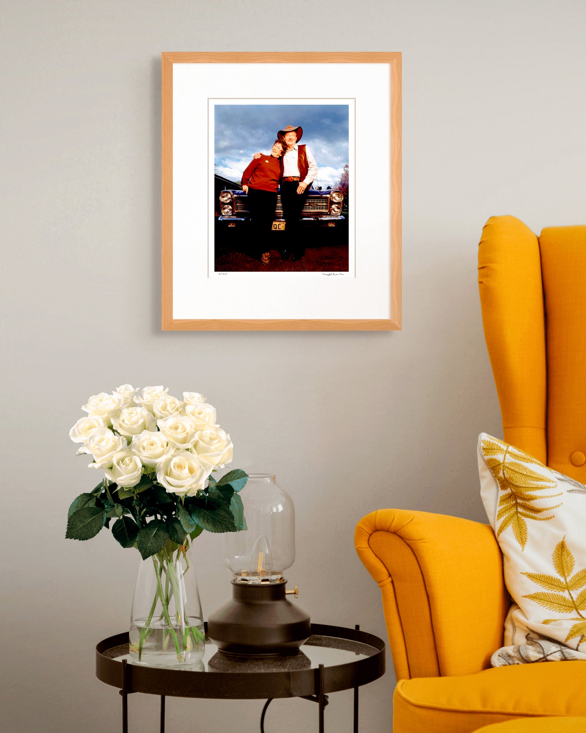 Framed Slim Dusty & Joy McKean photographic portrait styled with mustard yellow armchair and white roses – warm Australian interior design.