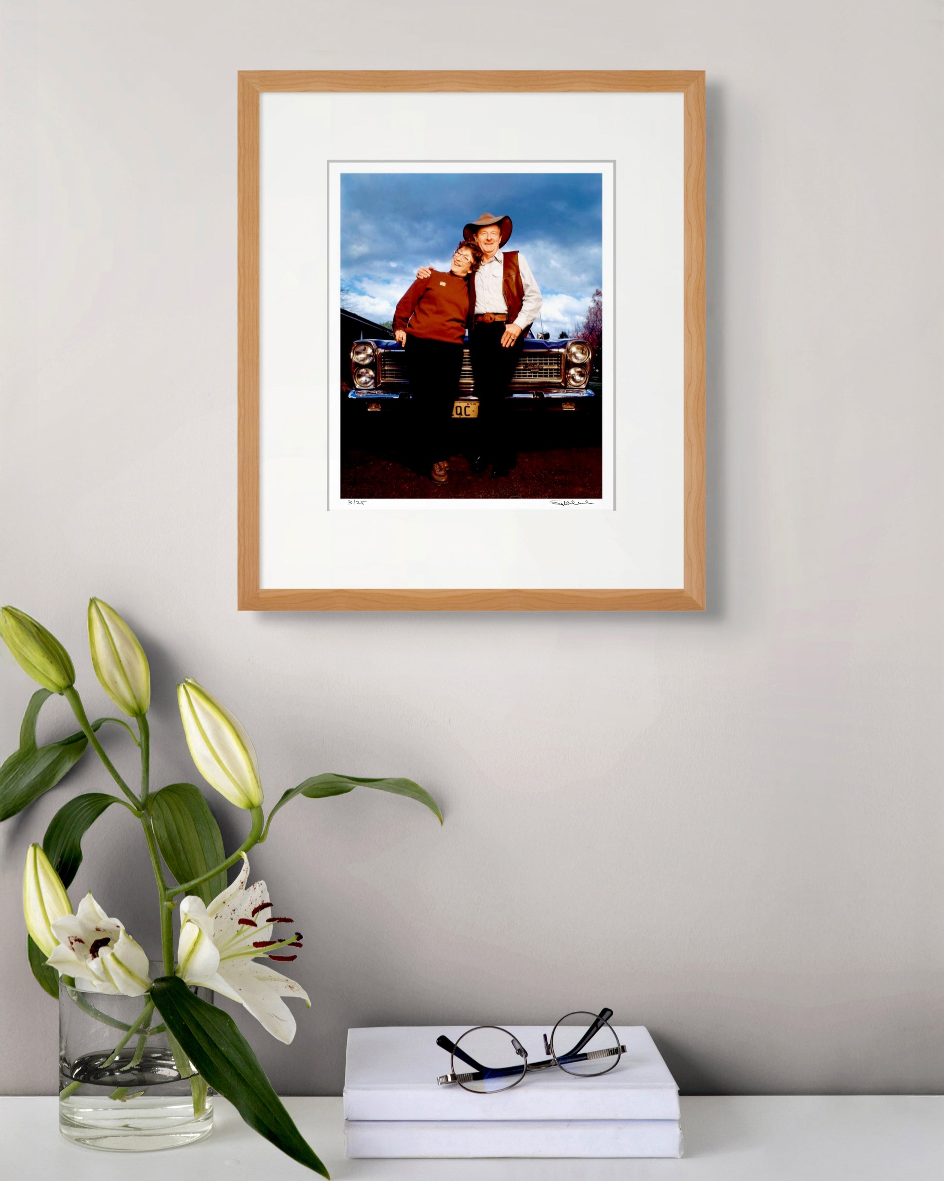 Framed Slim Dusty & Joy McKean portrait above white lilies and reading glasses – elegant, classic Australian photographic art.