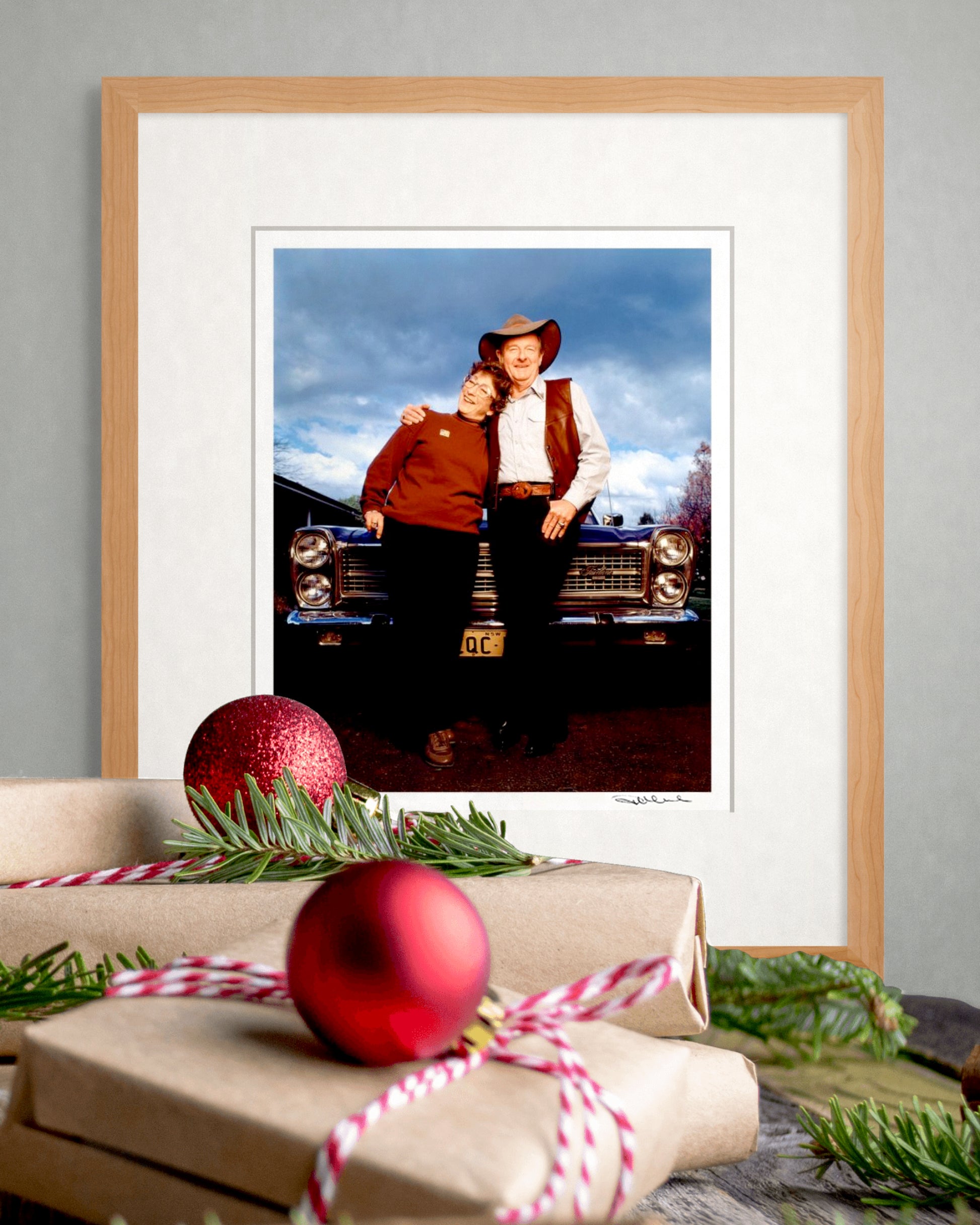 Framed limited edition Slim Dusty & Joy McKean portrait by Robin Sellick beside wrapped gifts and red Christmas ornaments – ideal collector’s gift edition.